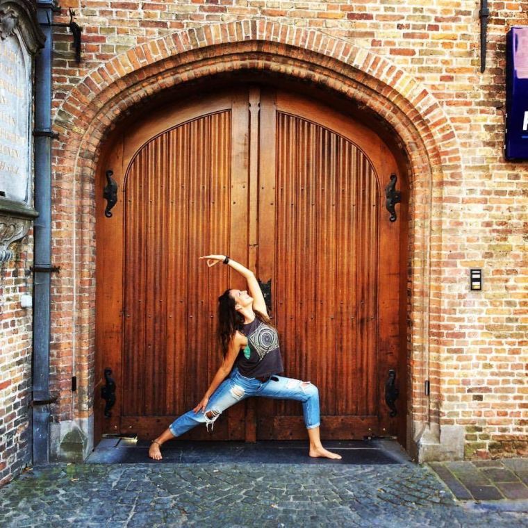 Friederike Döll in einer Yoga-Pose vor einem großen, geschlossenen alten Holztor, das zu einem Reiterhof führt.